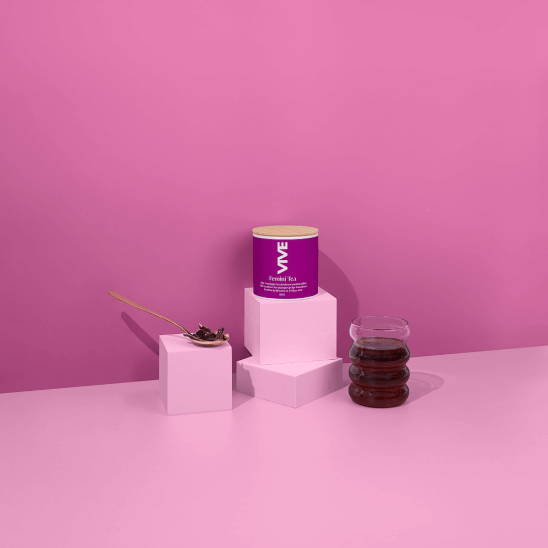 Femini Tea canister with a cup of tea, elegantly displayed on white pedestals against a pink backdrop.
